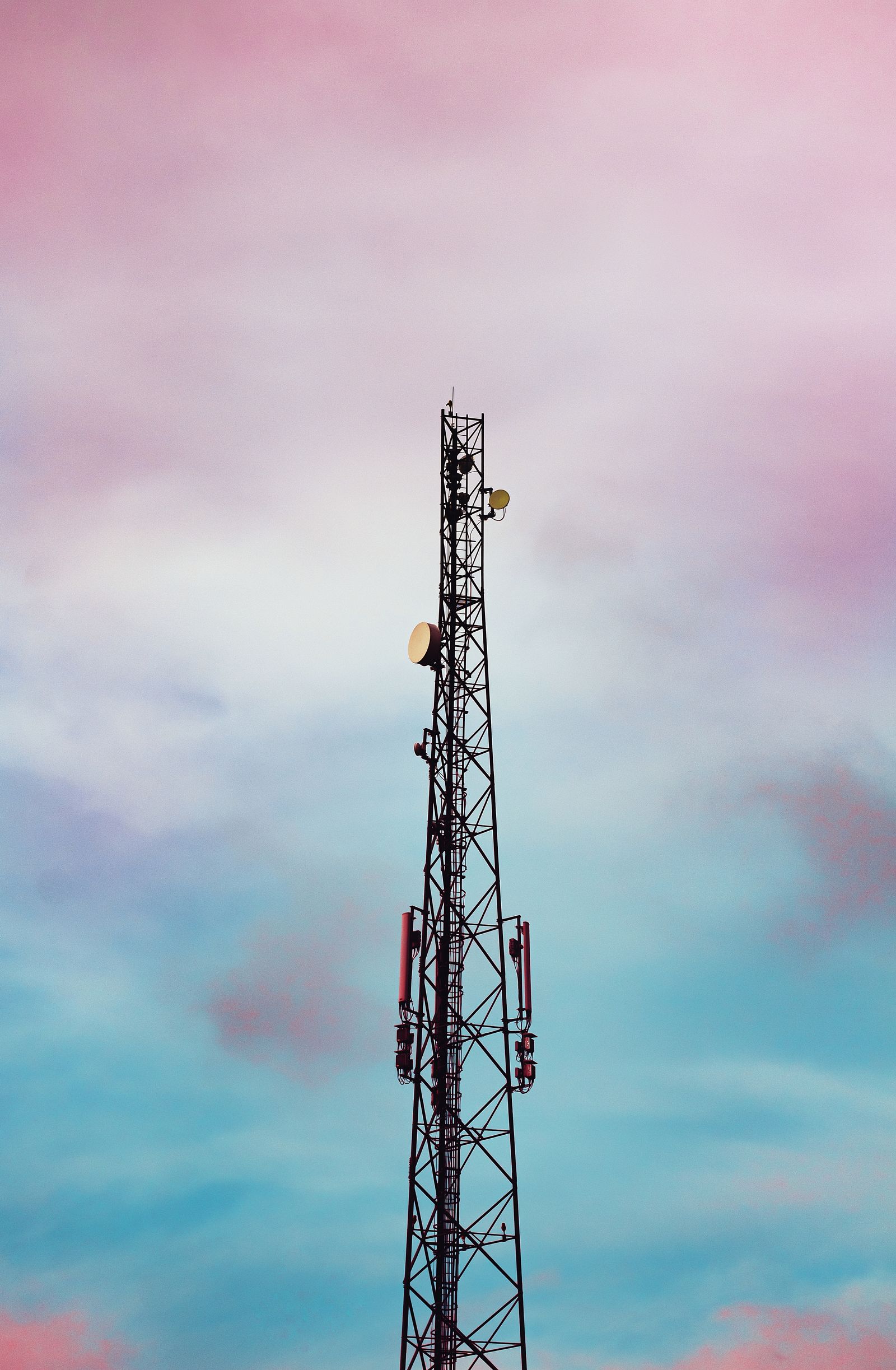 Torre de telecomunicações alta, com antenas, contra um céu rosa e azul.