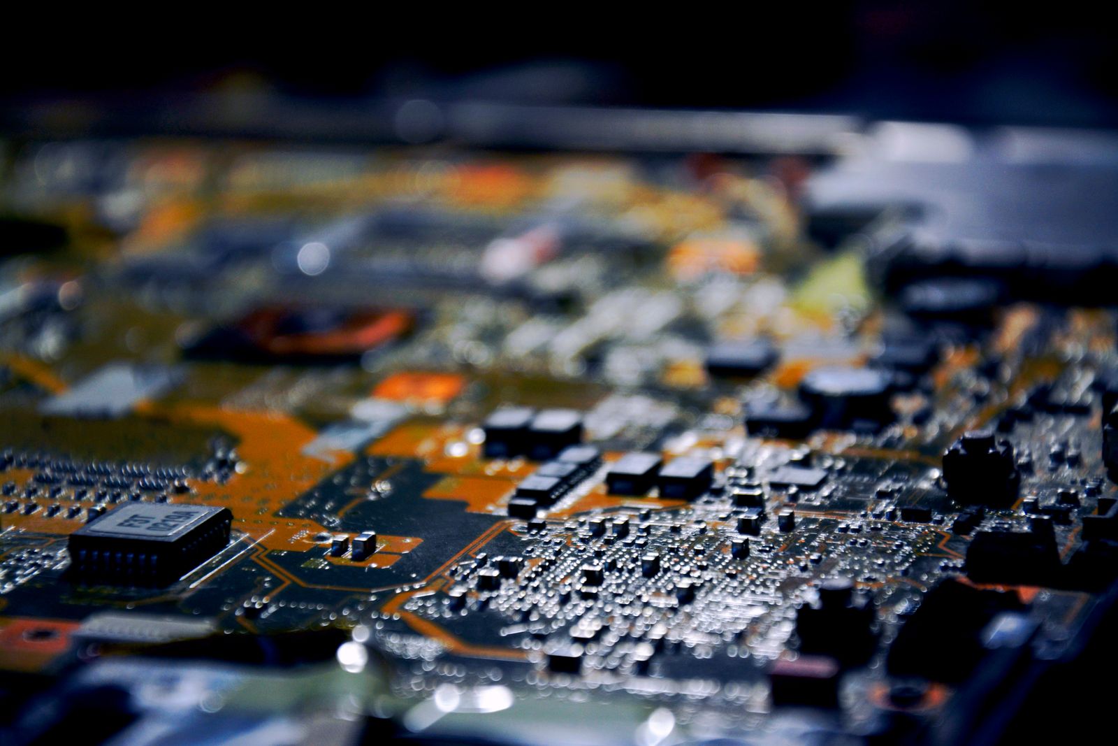 Close desfocado de uma placa de circuito com chips e componentes pequenos sob luz baixa.