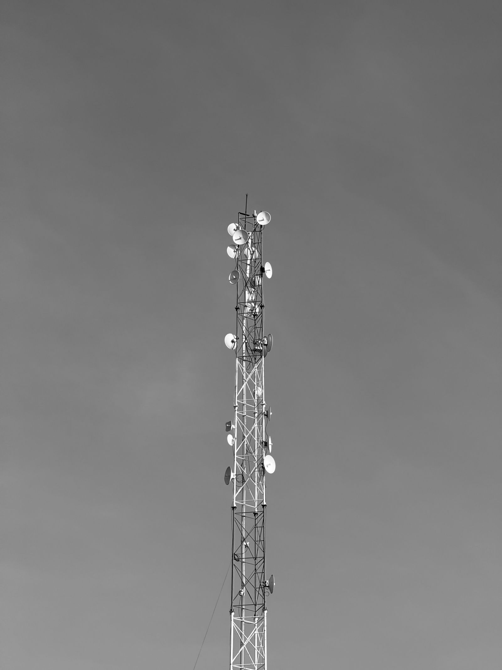 Torre de rádio treliçada com várias antenas parabólicas contra um céu cinza, em preto e branco.